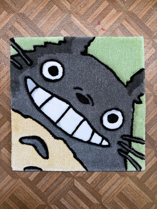 Tufted rug of Totoro, smiling and seen close up - only his face - with a mint green background.