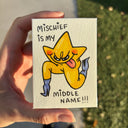 A hand holds a small artwork of a cartoon star character in yellow with blue boots and a pink tongue sticking out, with the text 'MISCHIEF IS MY MIDDLE NAME!!!' in black lettering.