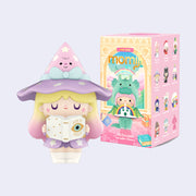 Vinyl figure of a girl dressed as a witch in light pinks and purples, reading a Book of Spells. She stands in front of the blind box packaging.