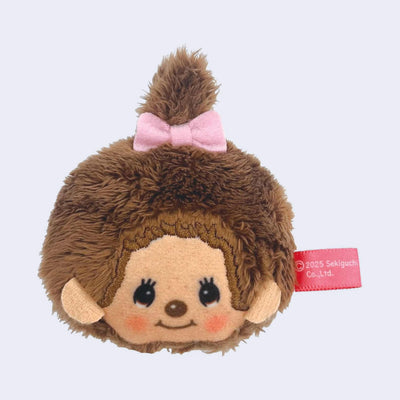 Plush face of a Monchhichi girl, a cute monkey with cartoon eyes and rosy cheeks. It has a tag coming out of the side of it.