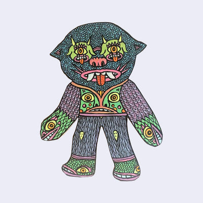 Die cut wooden sculpture of a small blue monster with knit clothing, with snake heads for mittens and shoes. It wears a pair of glasses that are cyclopses. 