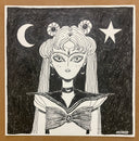 A black and white ink illustration of a stylized Sailor Moon-like character on a square piece of paper, photographed against a tan surface. The artwork shows a crescent moon, star, and circular hair ornaments in a monochrome hand-drawn style.