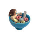 Ceramic sculpture of a nude girl, smiling and sitting inside a blue cereal bowl with Fruit Loops around her. She has a peaceful, closed eye expression.