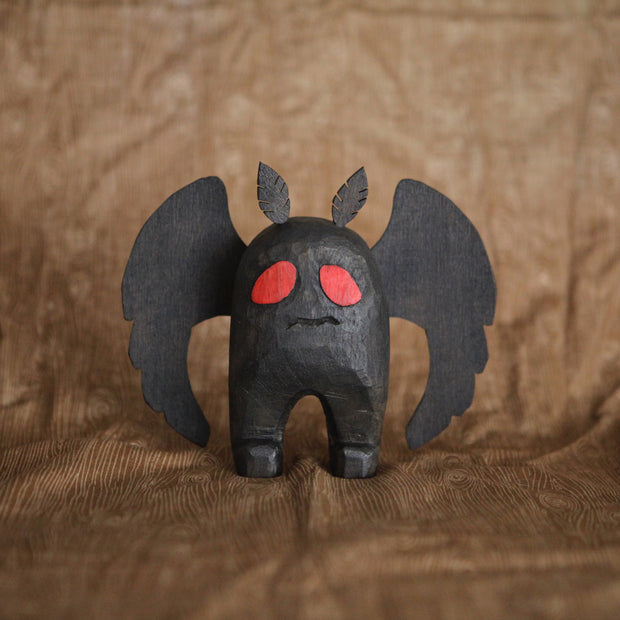 Sculpture of Mothman, the folklore legend, all black with a stout body and large flat wings. Its eyes are red and it has a simple disgruntled expression on its face.