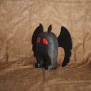 Sculpture of Mothman, the folklore legend, all black with a stout body and large flat wings. Its eyes are red and it has a simple disgruntled expression on its face.