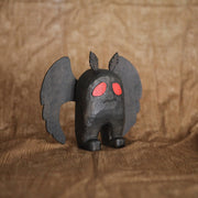 Sculpture of Mothman, the folklore legend, all black with a stout body and large flat wings. Its eyes are red and it has a simple disgruntled expression on its face.