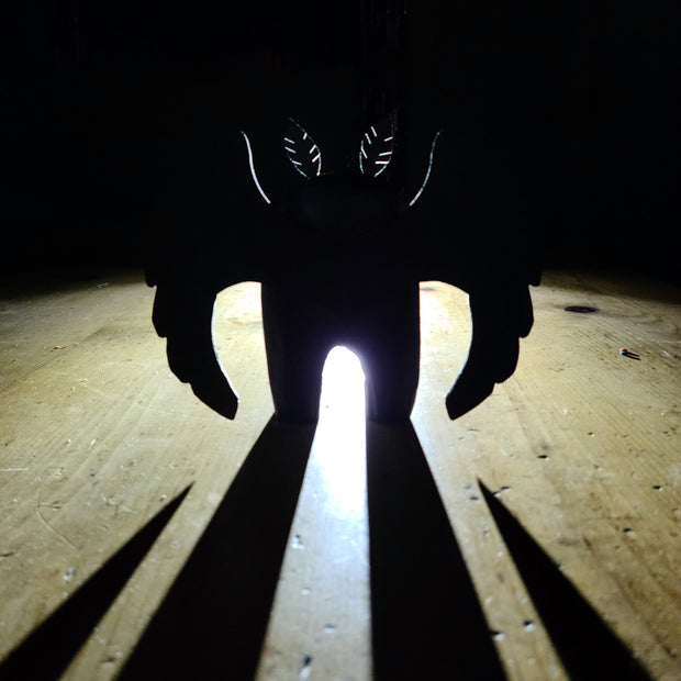 Sculpture of Mothman, the folklore legend, stylistically lit up from the back, casting a very large looming shadow despite its small size.