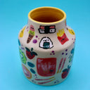 Ceramic vase with many small doodles on it of snacks, such as: fruit, fries, ice cream, cookies, rice snacks, donuts and pie.