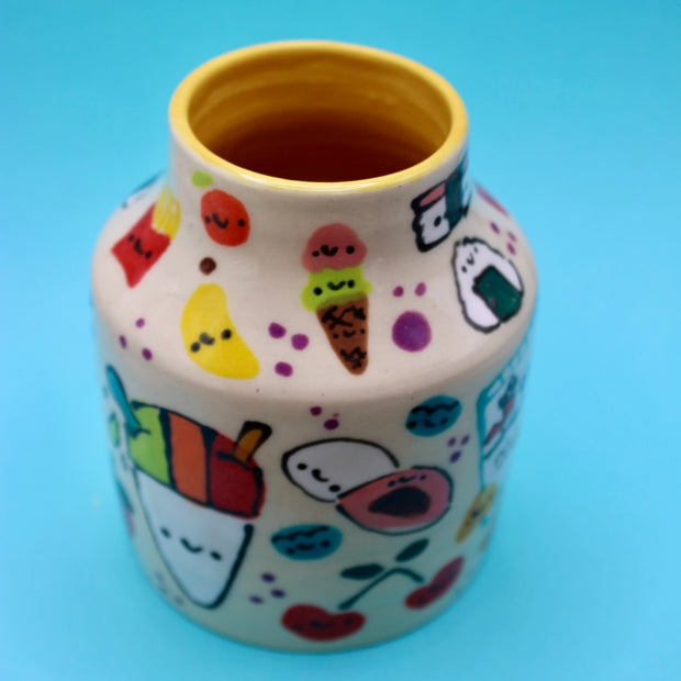 Ceramic vase with many small doodles on it of snacks, such as: fruit, fries, ice cream, cookies, rice snacks, donuts and pie.