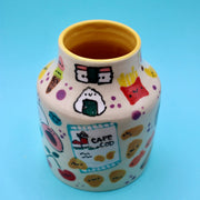 Ceramic vase with many small doodles on it of snacks, such as: fruit, fries, ice cream, cookies, rice snacks, donuts and pie.