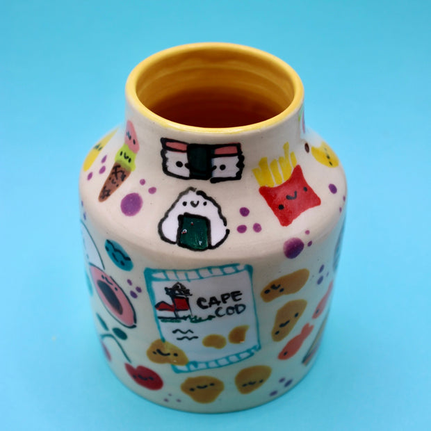 Ceramic vase with many small doodles on it of snacks, such as: fruit, fries, ice cream, cookies, rice snacks, donuts and pie.