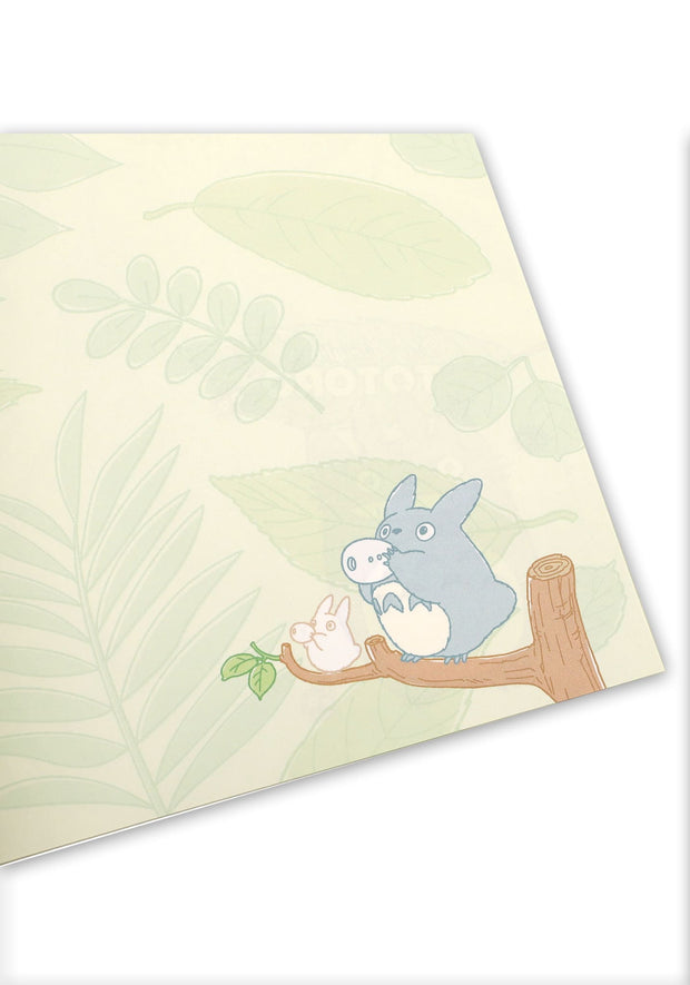 Notebook interior with green leaf patterned pages and 2 small Totoros on a branch playing a wind instrument.