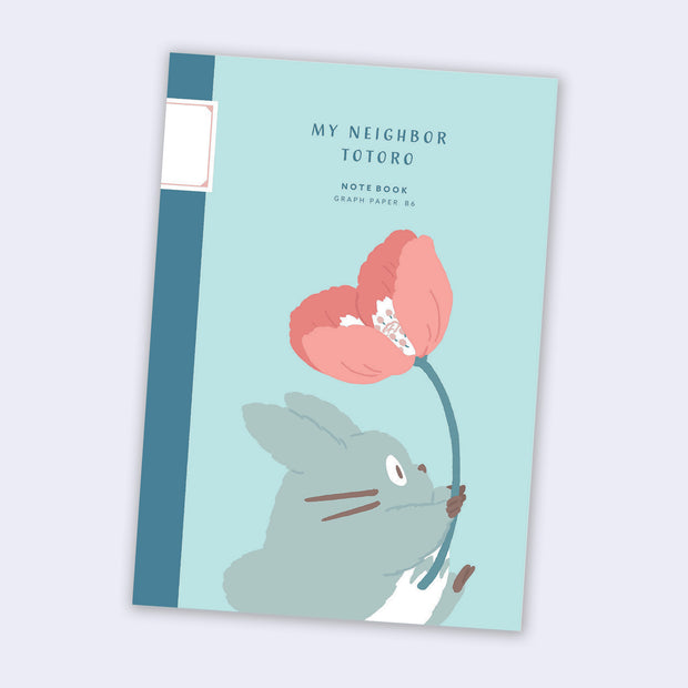 Teal cover notebook with a small Totoro holding a pink flower and walking.