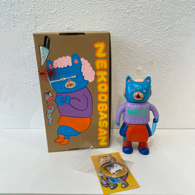 Blue painted soft vinyl figure of a cat headed humanoid with light pink hair, wearing a purple sweater that says "neko" and a blue skirt with a red frilly apron. She holds a blue knife.
