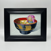 Framed artwork of a fish-like character with pink hair in a bowl of soup on a textured background