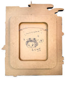 MDF cutout with a small drawing of a character and text inside a rectangular frame.