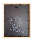 Back of a framed artwork with a white line drawing of a character and signature.