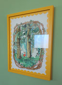 A framed artwork featuring a whimsical forest illustration with a yellow frame, hanging on a sage green wall.