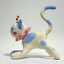 Ceramic figurine of a white cat with blue spots, wearing a pink ruffled collar, a small clown hat with clown makeup.
