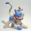 Ceramic figurine of a white cat with blue spots, wearing a pink ruffled collar, a small clown hat with clown makeup.
