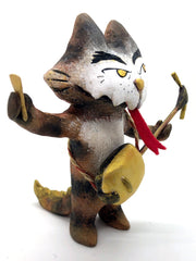 Painted sculpture of a cat with a white dripping face, gold eyes and nose. In one hand it holds the neck of a 3 stringed instrument slung around its body and the other holds a pick. A forked red tongue comes out of its mouth.
