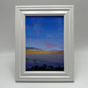 Landscape painting of a seaside view at sunset, with a mostly dark blue sky and an orange setting sun. Trees can be seen at the bottom of the scene. Piece is framed.