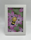 Painting of a cartoon bee laying amongst pink flowers. Piece is framed.
