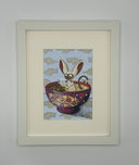 Framed artwork featuring a cartoon lemur sitting inside a decorated purple bowl, mounted with a wide cream mat on a light gray wall.