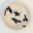 Ceramic plate with black bird illustrations on a beige background
