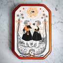 Black ink illustration with subtle orange coloring of 2 small girls in black dresses, with one hand on the other's face. The back of their hands have an eye on them. A doll head with long braids is at the bottom of the piece, with the braids framing the scene.