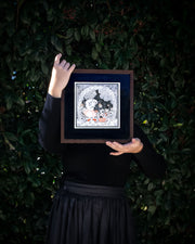 Piece of art being held in the hands of the artist, standing against a green bush.