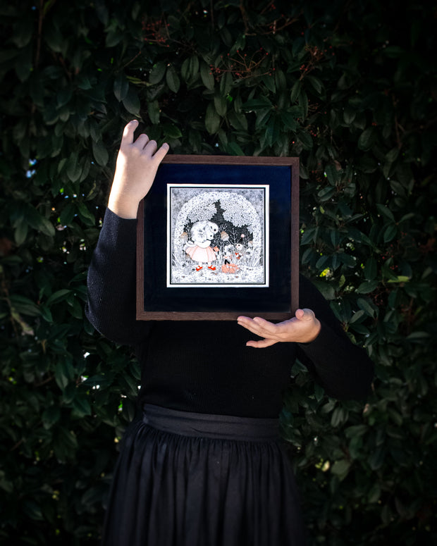 Piece of art being held in the hands of the artist, standing against a green bush.