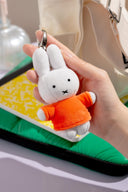 White plush bunny keychain with an orange shirt held by a hand against a blurred background
