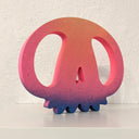 Pink and purple wooden sculpture of a skull, with large eye sockets and rounded nubs for teeth.