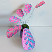 Sculpture of a plant made out of pink and blue risograph printed paper leaves, attached by wire to a pot. Leaves have a rounded striping pattern.