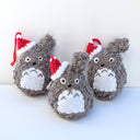 Group of small crocheted Totoros, all with red Santa hats hanging on one of their ears. 