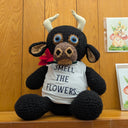 Crocheted bull with a shirt that says "smell the flowers" and a red flower in its mouth.