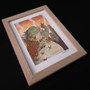 Framed artwork of a green creature with butterflies against a cityscape background