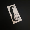 A minimalist black and white drawing featuring a stylized figure and a dark abstract shape, photographed at an angle on a dark background.