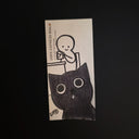 A rectangular drawing of a black-and-white cartoon illustration of a child at a desk and a large cat face, photographed on a dark black background. Visible text includes 'POST EXPRESS MAIL' and 'POST EXPRESS MAIL POST'.