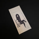 A rectangular cream-colored drawing featuring a minimalist black ink illustration of two stylized figures, photographed at an angle on a solid black background.