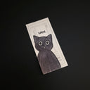 A rectangular black cat illustration with large white eyes, placed on a dark black background. The card has a white border and partial text including 'MEH.'