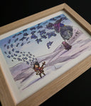 A framed artwork featuring a whimsical illustration of a small figure with a stringed instrument, floating paper coming off of it, a large gray statue, and a purple bird, displayed in a light wood frame against a black background.