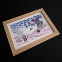 A framed artwork featuring a whimsical illustration of a small figure with a stringed instrument, floating paper coming off of it, a large gray statue, and a purple bird, displayed in a light wood frame against a black background.