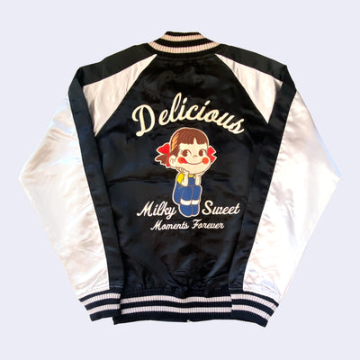 Shiny polyester bomber jacket with black body and white sleeves. Back has a large embroidery of Peko Chan, sitting with her elbows on her knees and smiling. Text around her reads "Delicious Milk Sweet Moments Forever"