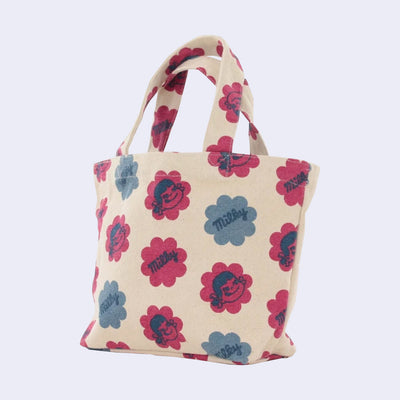 Cream colored purse with a pattern of large flower shaped blocks of red and blue, faded stylistically. One diagonal row features illustrations of Peko Chan's smiling face, and the next row features text that reads "Milky" within the flowers. Row pattern alternates between designs.