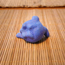 Small sculpture of a blueberry with a cute cartoon sad face - green eyes looking to the side and a frown with a single tear falling down. It lays on its side.