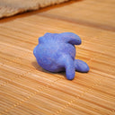Small sculpture of a blueberry with a cute cartoon sad face - green eyes looking to the side and a frown with a single tear falling down. It lays on its side.