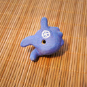 Small sculpture of a blueberry with a cute cartoon sad face - green eyes looking to the side and a frown with a single tear falling down. It lays on its side.