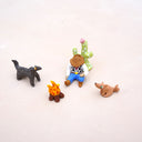 Set of miniature figurines including a cowboy, dog, cat, and cactus on a light background